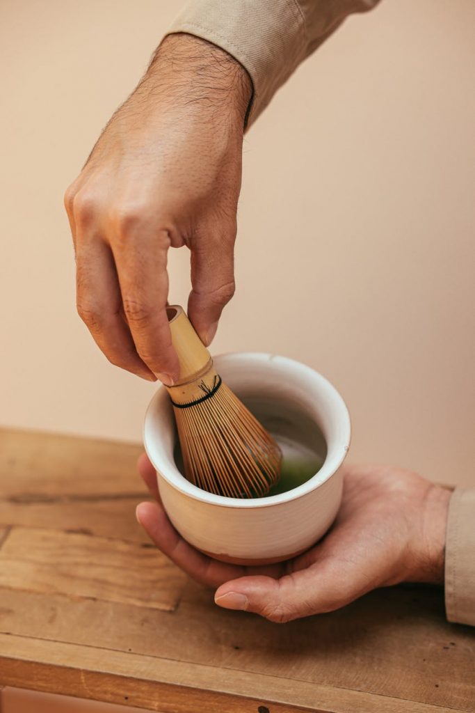 person mixing green tea on ceramic bowl